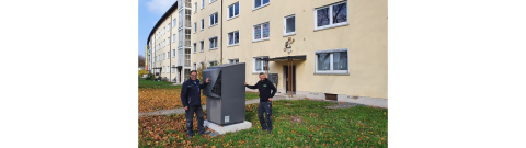 Zwei Installateure neben Dimplex-Wärmepumpe vor Mehrfamilienhaus